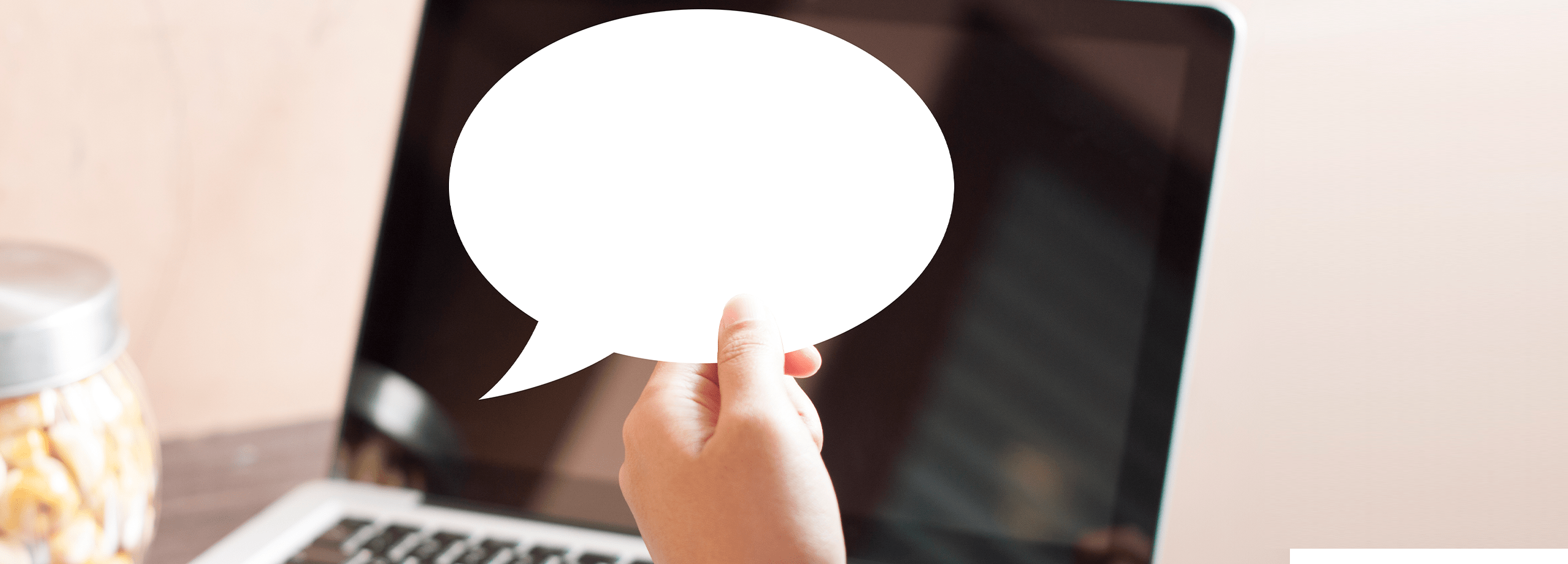 Photo of a hand holding a speech bubble in front of a laptop